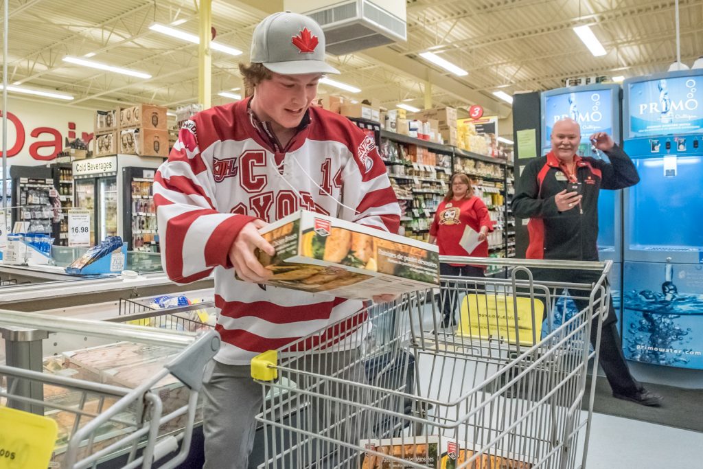 Coyote Captain Rainer Glimpel quickly filled a grocery cart with boxes of mean products during a 50-second shopping spree at Buy-Low Foods while Manager Brian Fry (right) looks on. Glimpel was filling in for spree winner Kay Patterson, who is unable to run. (Richard McGuire photo)