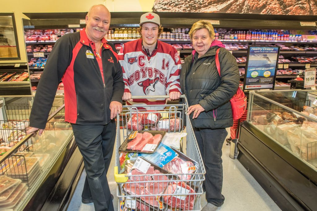 Kay Patterson, right, won a 50-second shopping spree at Buy-Low Foods, but since she is unable to run, she asked Osoyoos Coyotes Captain Rainer Glimpel to do the legwork. He filled the cart with about $500 in meat products. At left is store manager Brian Fry. (Richard McGuire photo)