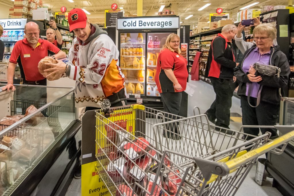 Osoyoos Coyotes Captain Daniel Stone loads his shopping cart with meats as he does the legwork for Joanne Patterson (right), who won a one-minute shopping spree at Buy-Low Foods Thursday. Patterson instructed Stone on what she wanted him to grab -- the most expensive meats -- and she was pleased with the job he did. While Stone is fast on the ice, he normally is a slow shopper who takes his time pondering what to buy. So this was a new experience for him. (Richard McGuire photo)