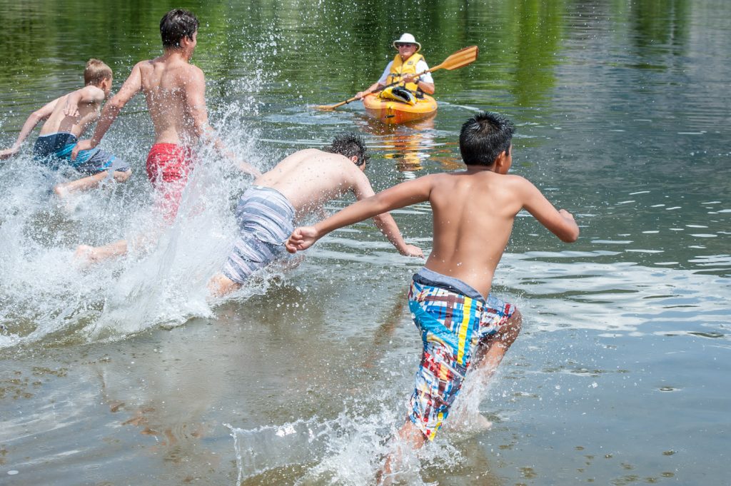 Students Jason Lynch, Jaedan Holz, Cole Rezka and Antonio Mora plunge into the lake to begin the swimming portion of a relay that ends with scaling a wall. (Richard McGuire photo)