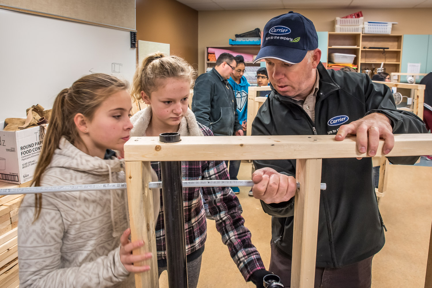 Jada Gaudet and Lianne Shiels, both in Grade 7 at Osoyoos Elementary School, watch as Brian Zakall of Joe's Plumbing shows them how to insert a pipe through holes they've drilled. The students had an introduction to various building trades last week. (Richard McGuire photo)