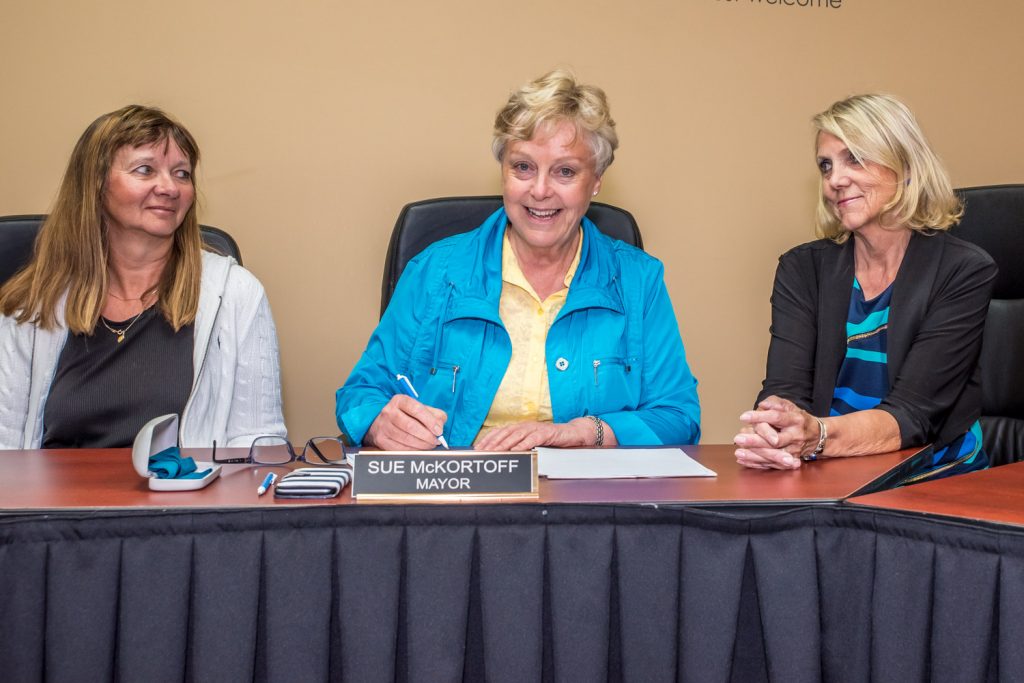 Mayor Sue McKortoff signs the order proclaiming May 21 to be Osoyoos Lake Appreciation Day. The event is organized by the Osoyoos Lake Water Quality Society to raise awareness of the lake and water issues. At left is Lyn Motkoski, a member of the committee for the event, and at right is Birgit Arnstein, president of the OLWQS. (Richard McGuire photo)