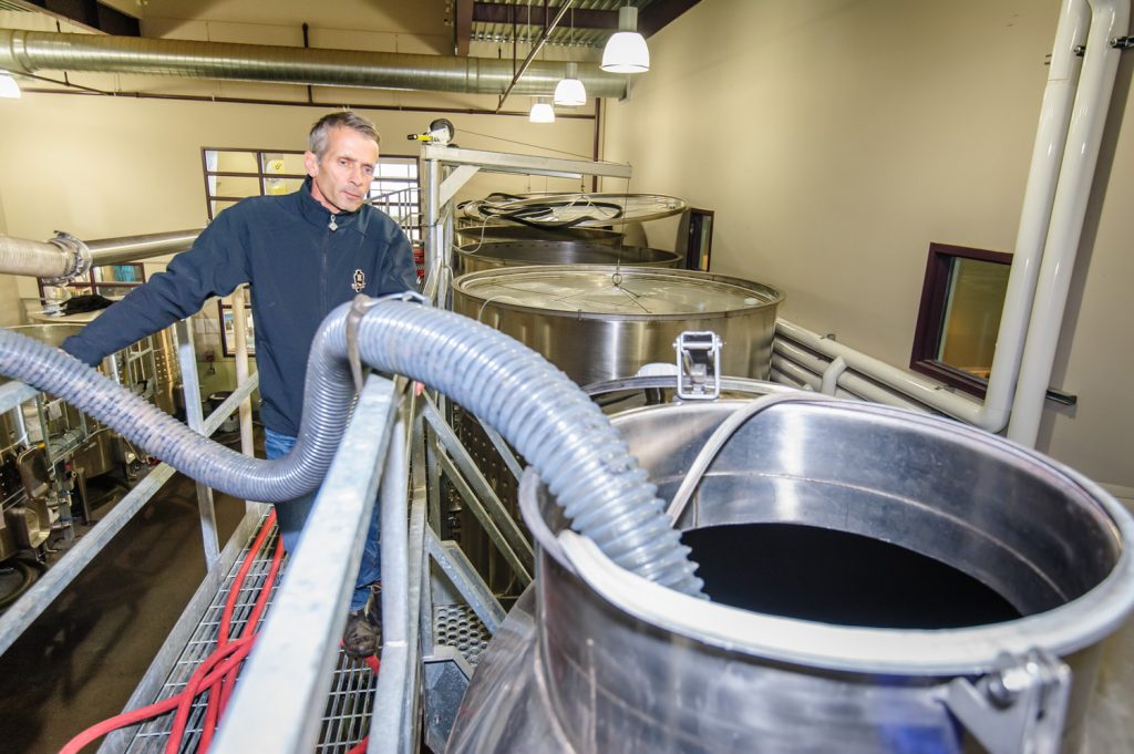 Randy Picton (left), winemaker at Nk'Mip Cellars, looks on as a hose empties fresh grape juice into a tall steel storage tank in this file photo taken during harvest last year. (Richard McGuire photo)