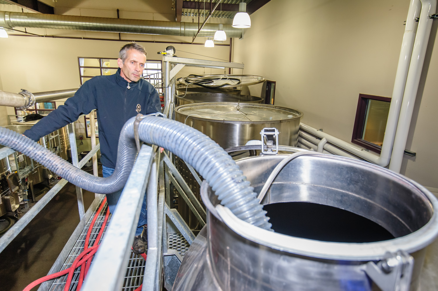 Randy Picton (left), winemaker at Nk'Mip Cellars, looks on as a hose empties fresh grape juice into a tall steel storage tank in this file photo taken during harvest last year. (Richard McGuire photo)