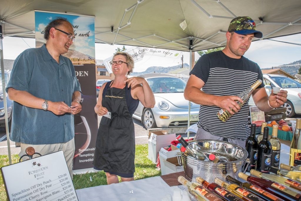 John Yap (left), the parliamentary secretary to B.C. Justice Minister Suzanne Anton, chats with Kim Brind'Amour, owner of Forbidden Fruit Winery, while her son Nathan Venables pours a sample for a customer. Yap has been responsible for reforming B.C.'s liquor laws, including the change that allows local producers of beer, wine and spirits to sell and sample their products at farmers' markets. He toured Market on Main in Osoyoos on Saturday to find out how the program is working for local winemakers. (Richard McGuire photo)